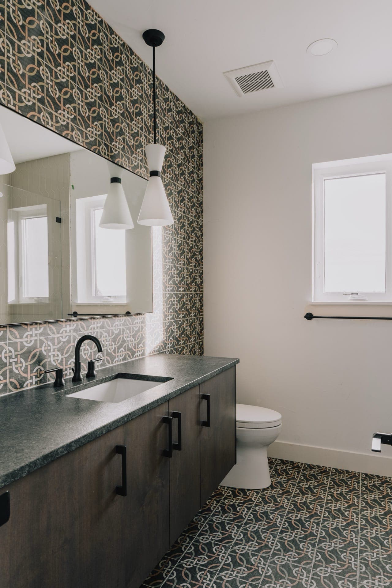 Bathroom with a double vanity, patterned tile and a window beside the toilet
