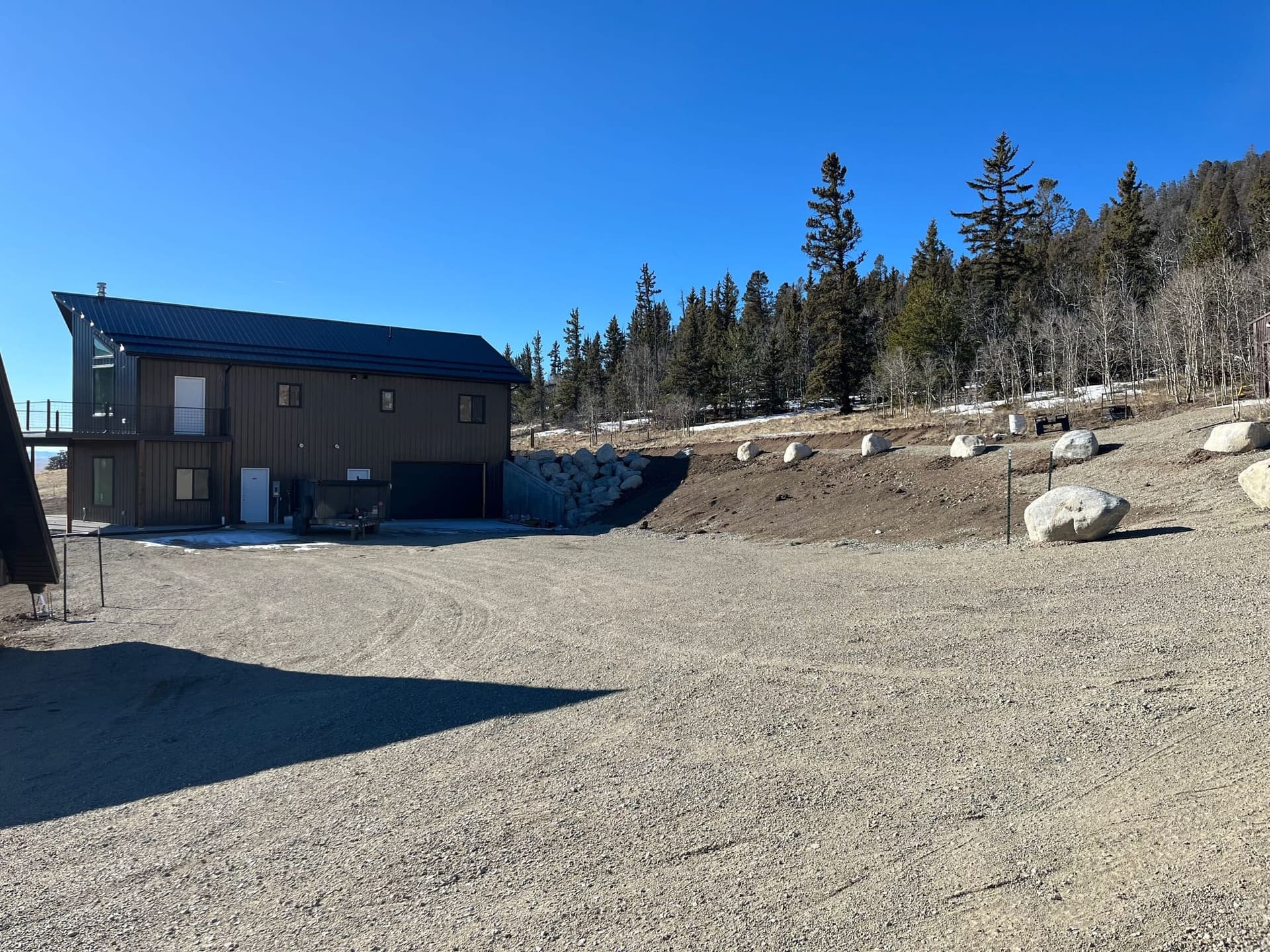 Dark metal siding with cedar post balcony, cable railing, and boulder retaining wall