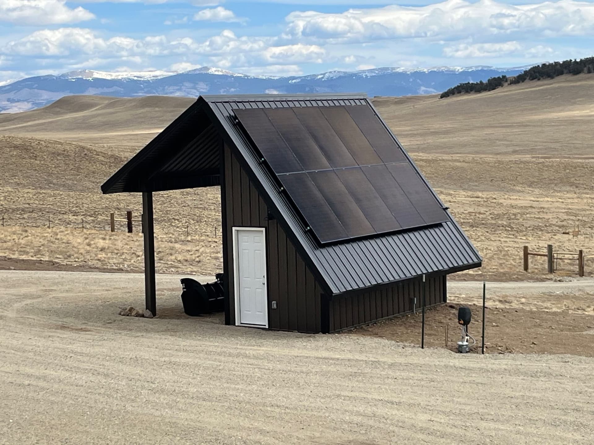 Dark metal solar panel shed with covered carport against snowy peaks