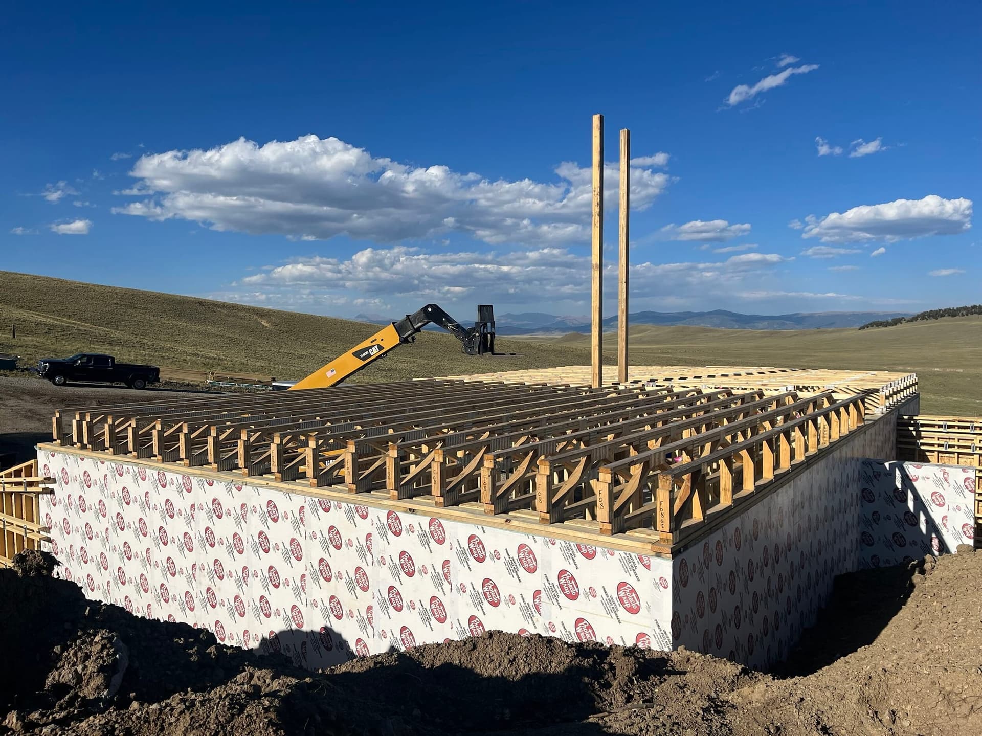 Floor framing across ICF foundation walls with construction equipment in the background