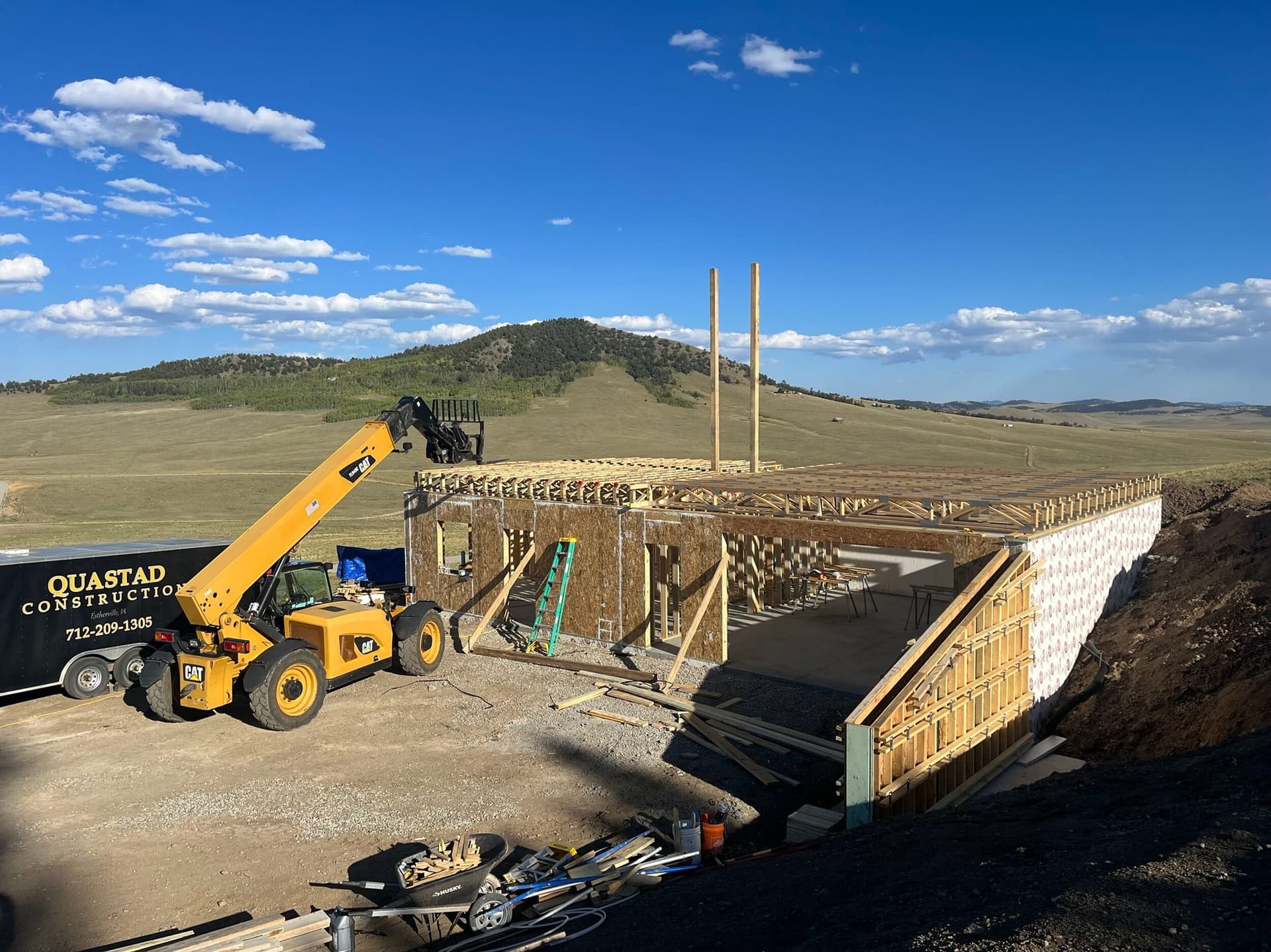 Wide view of the foundation and floor framing beside a telehandler on the mountain site