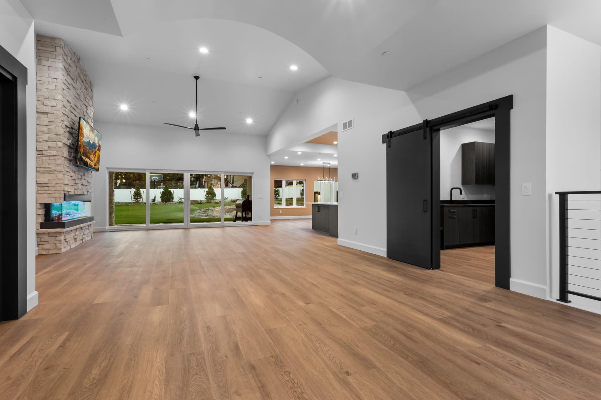 Great room toward the hall with a stone fireplace, sliding glass doors and a black barn door