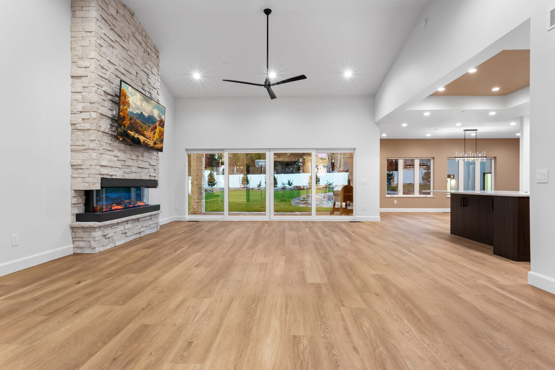 Great room wide view — open-concept layout, vaulted ceilings, stacked stone fireplace, kitchen beyond