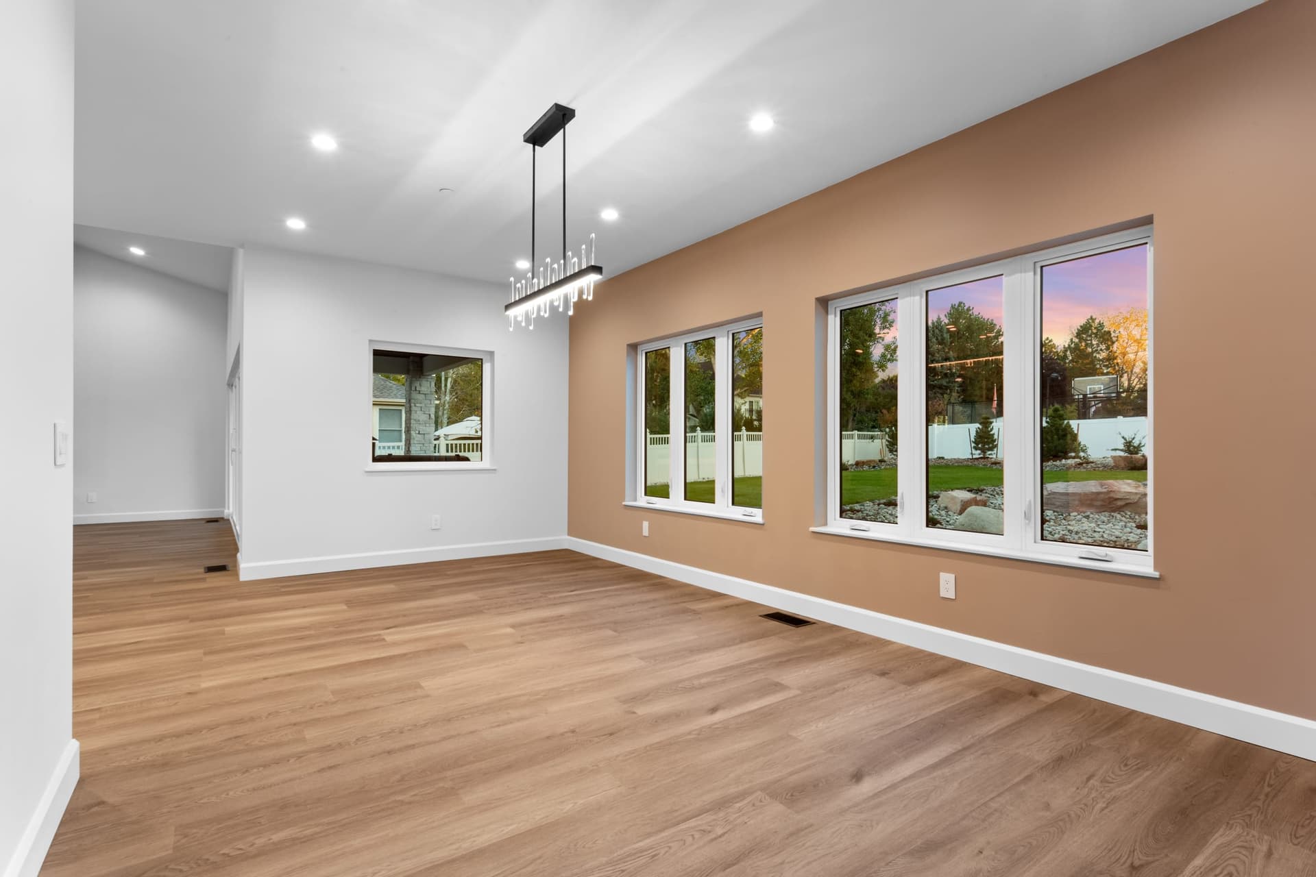 Dining area with a terracotta accent wall, linear chandelier and large windows