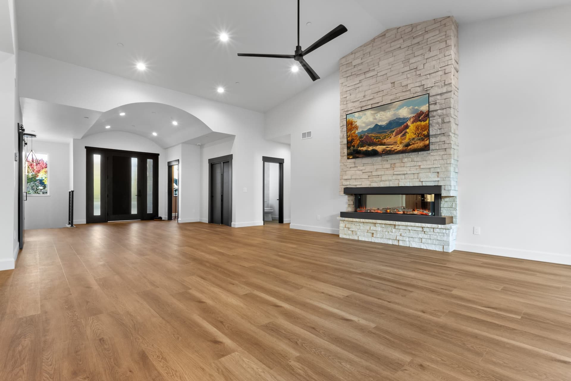 Living area toward front entry — barrel-vault foyer, black-framed double glass doors, stacked stone fireplace at right