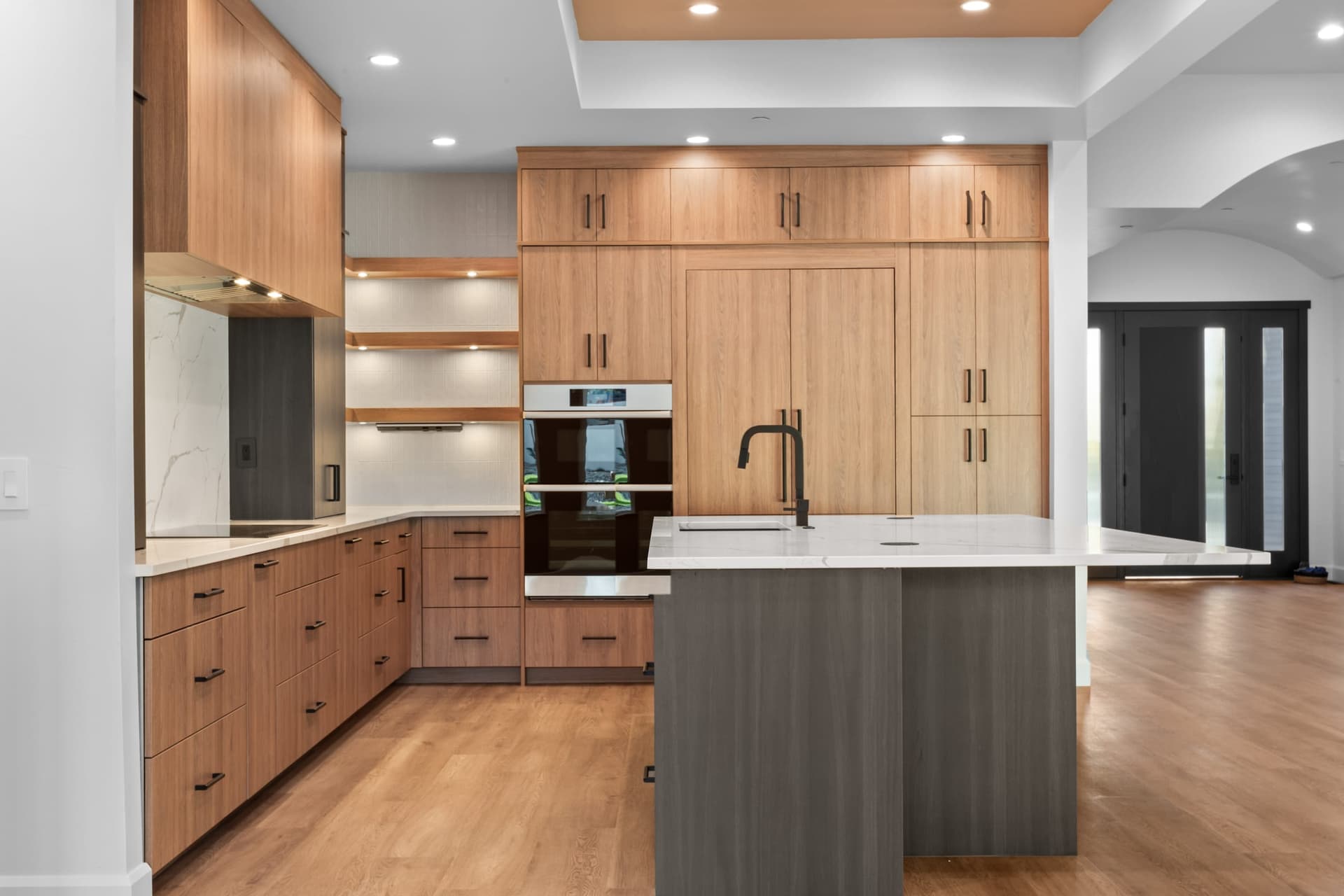 Appliance wall — walnut flat-panel cabinetry, floating wood shelves, double wall ovens, full-height calacatta backsplash