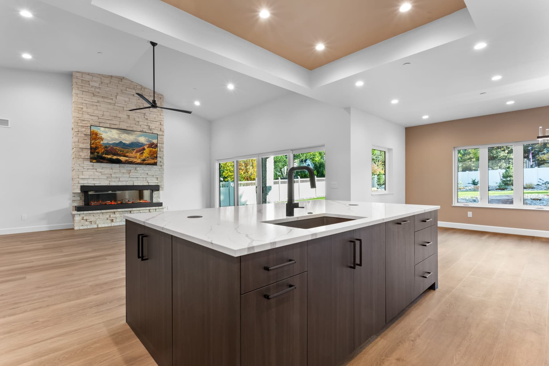 View from kitchen island into the great room — stacked stone fireplace, vaulted ceilings, sliding glass doors