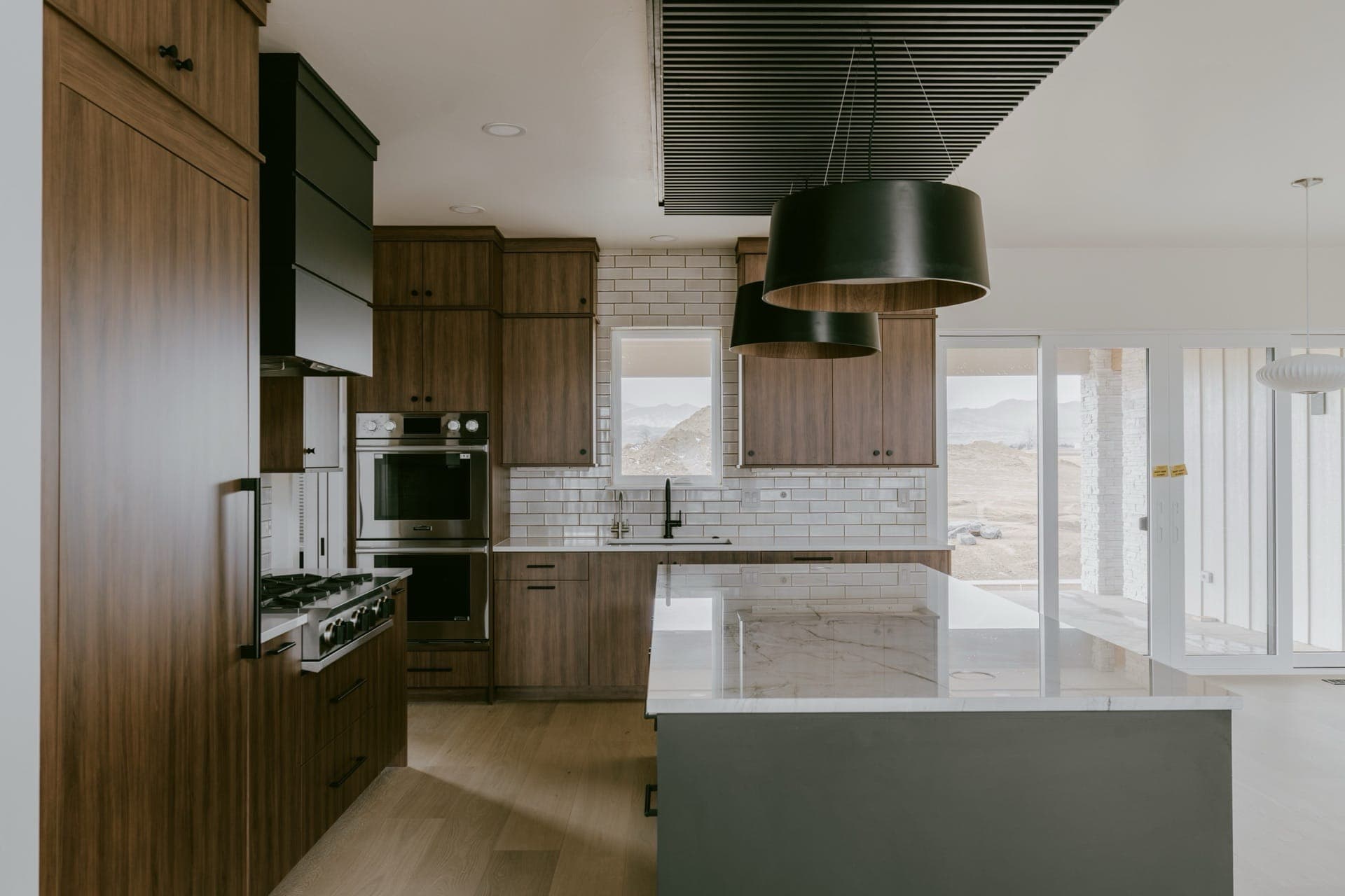 Kitchen island with dark pendant lights, wood cabinets and large windows