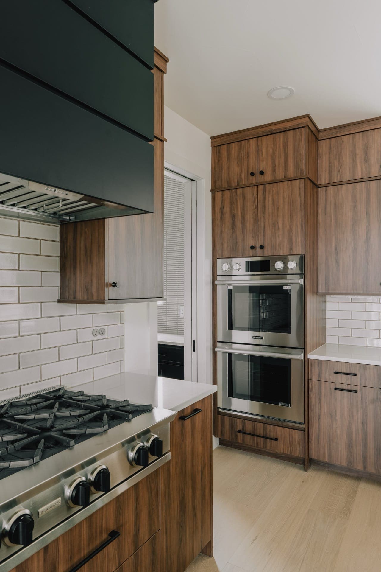 Kitchen range and stacked ovens with wood cabinets and a black hood