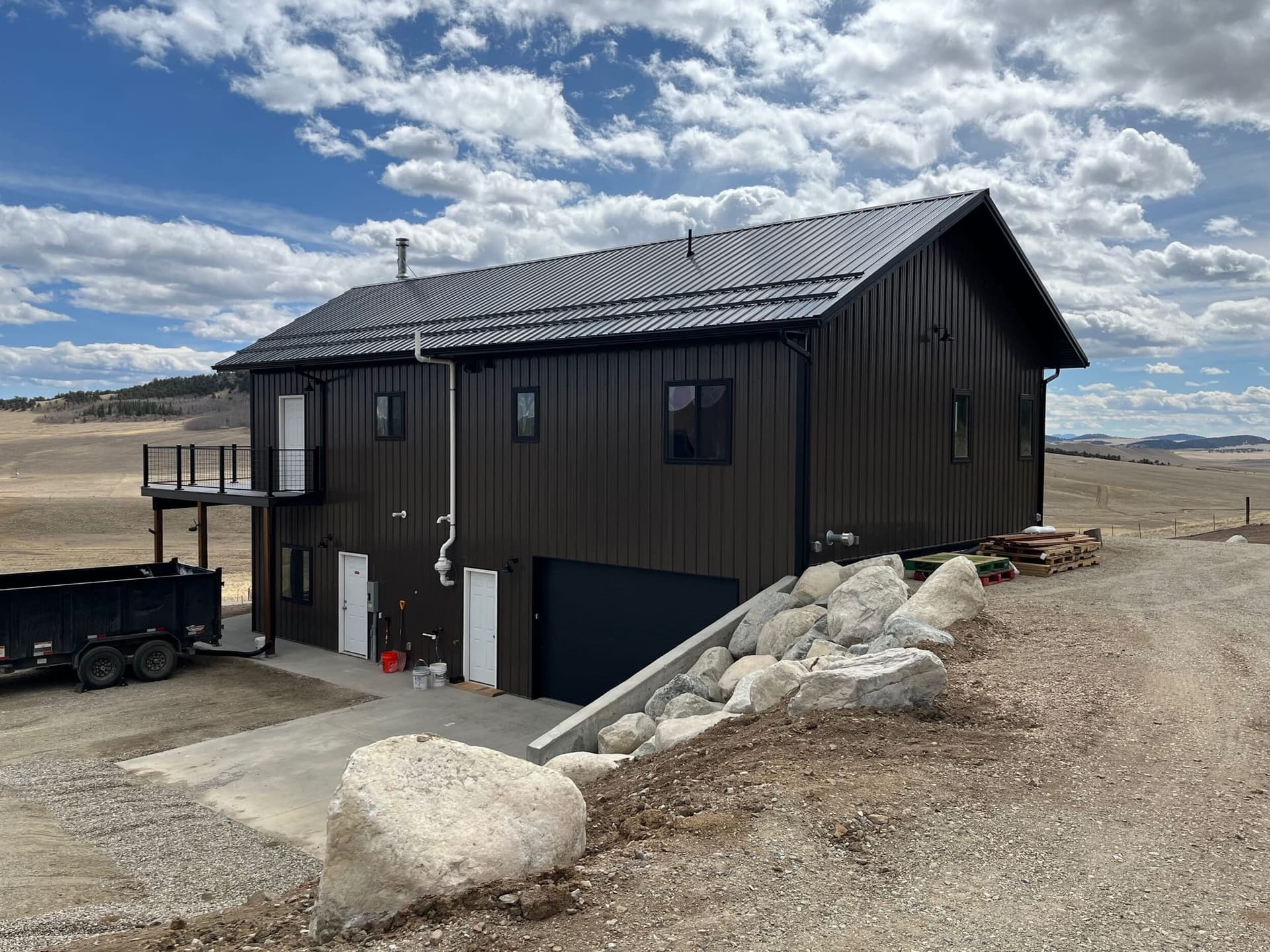 Side of a dark-sided mountain home with a sloping metal roof and large boulders