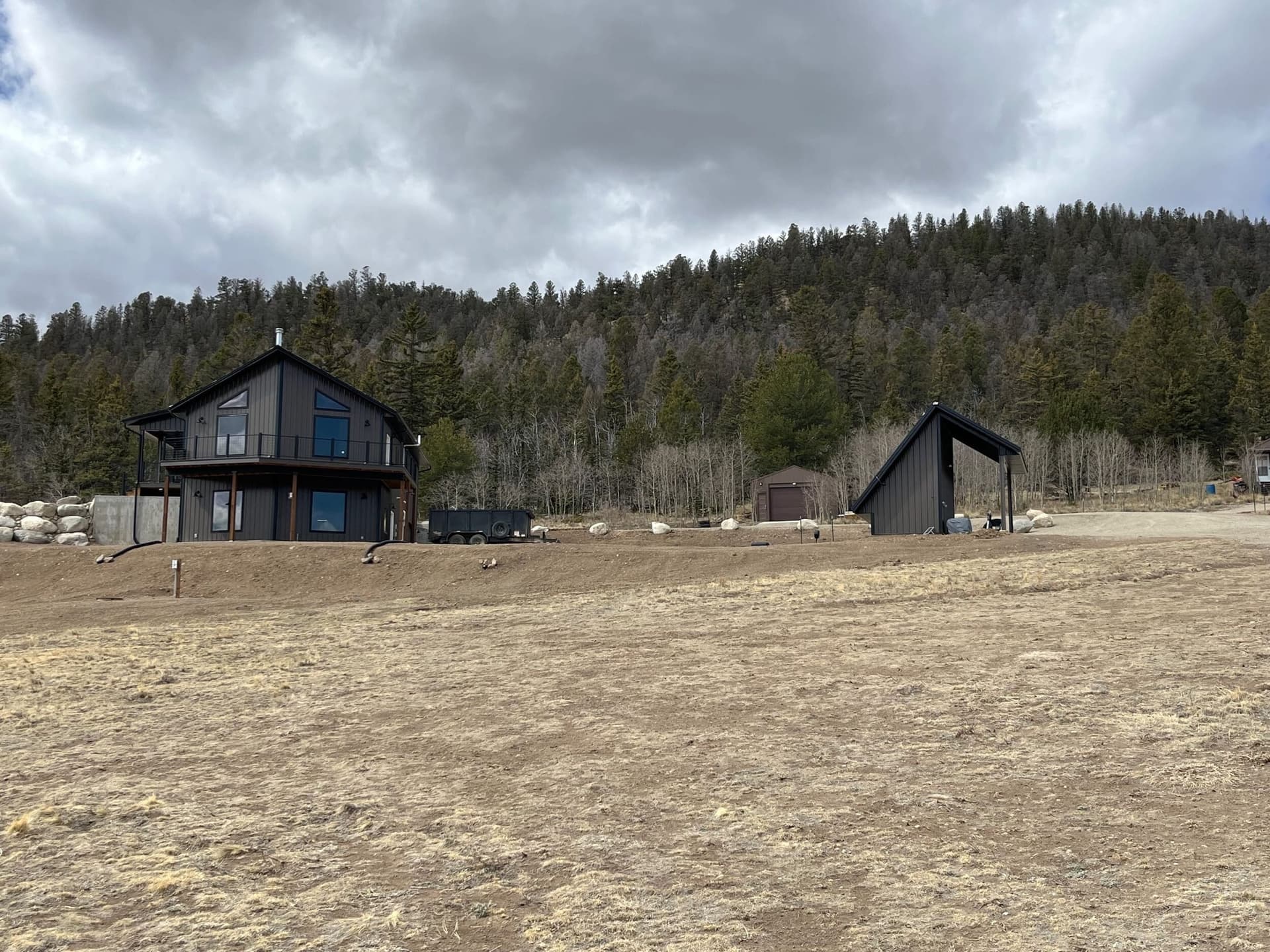 Mountain home across an open yard with a wooded hillside behind it