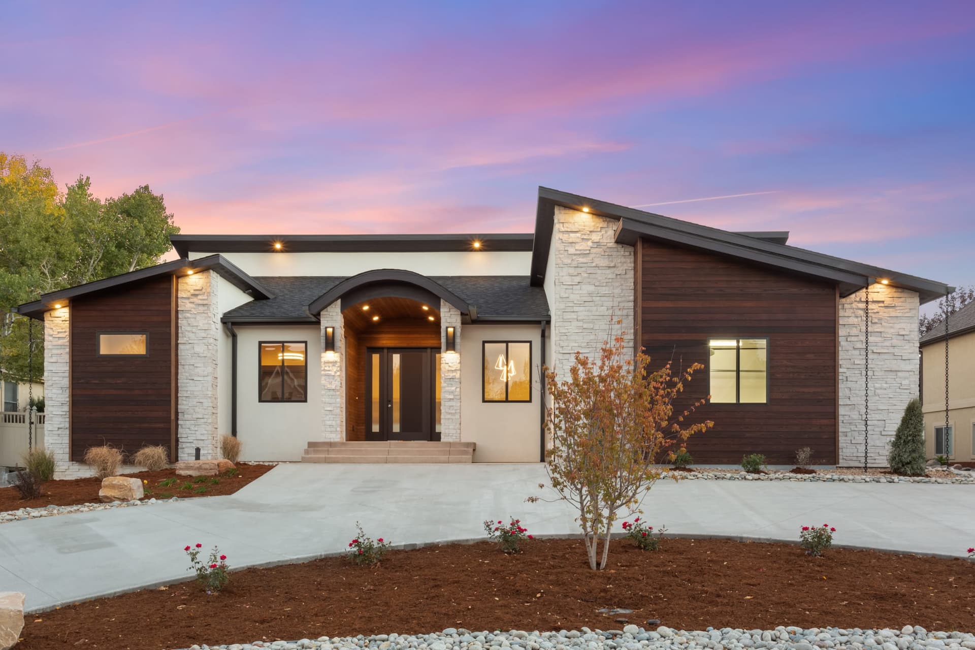 Ranch home front elevation with stone columns and an arched entry at twilight