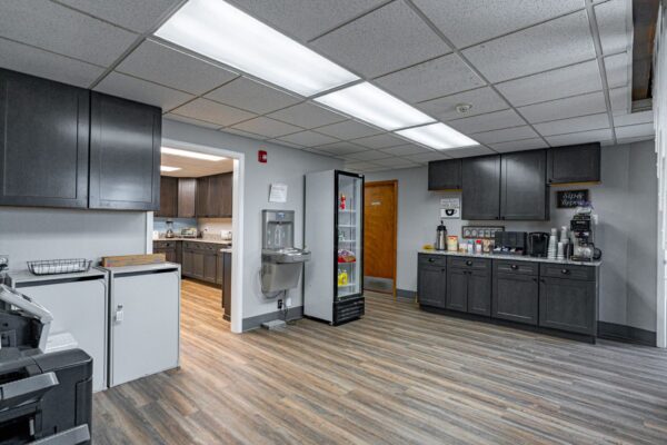 Commercial build featuring employee space with a corporate kitchen, large beverage refrigerator, storage for office supplies, hardwood flooring, and office products.