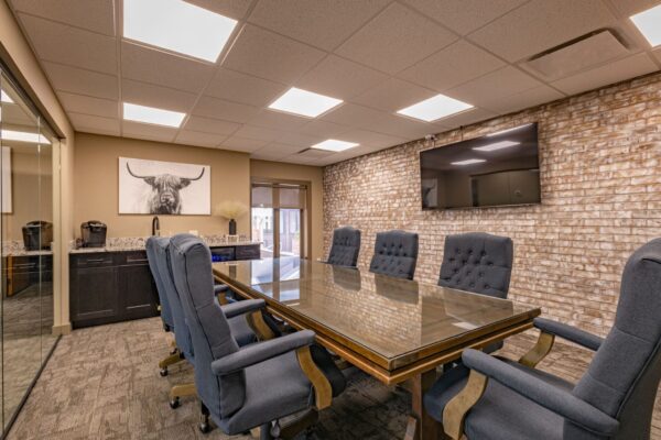 Commercial conference room with an elegant brick wall, tech setup, corporate kitchen, mirrored wall, and a large conference table with comfortable seating.