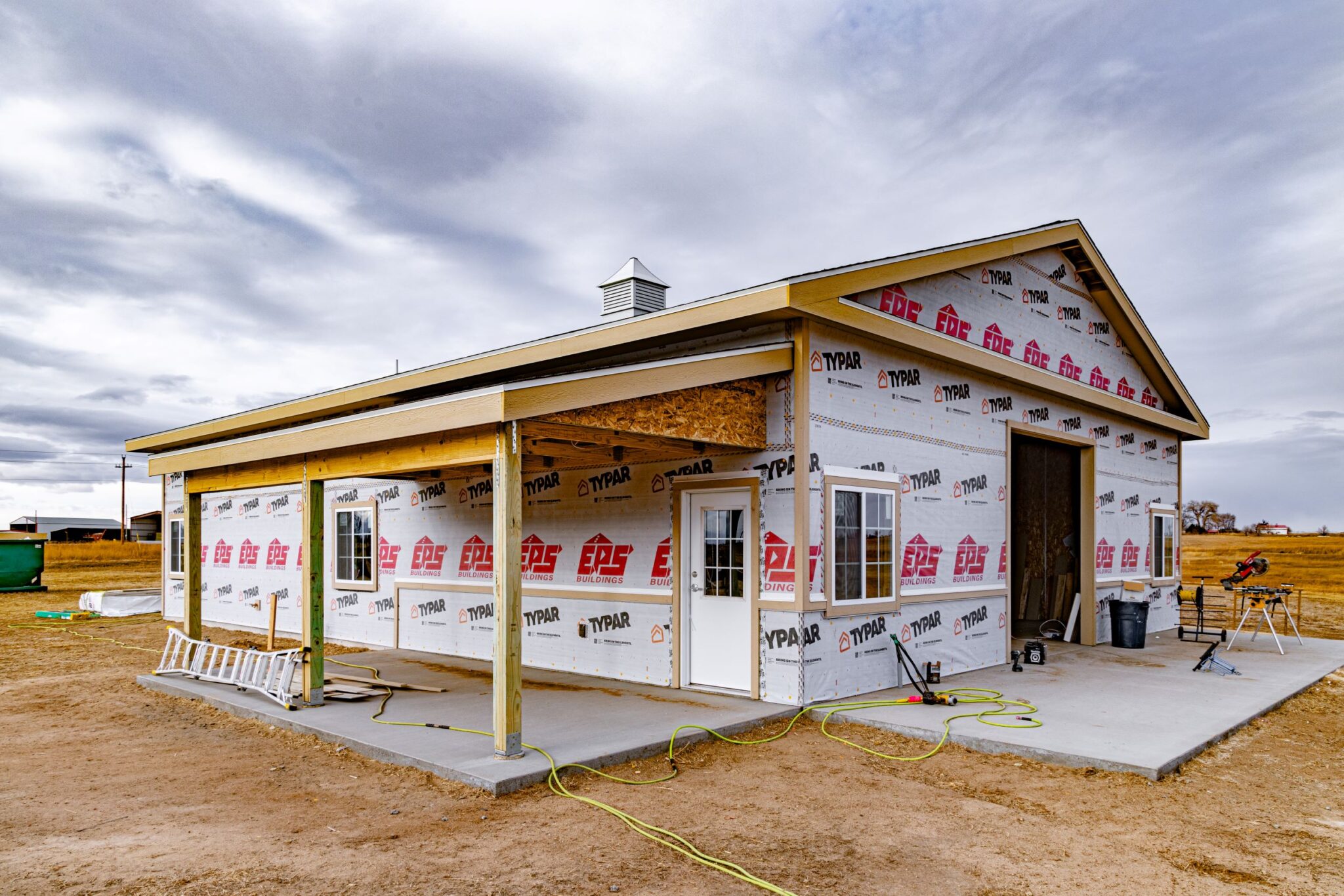 New build exterior image of barn framing with a porch, interior room, natural lighting, and commercial garage space.