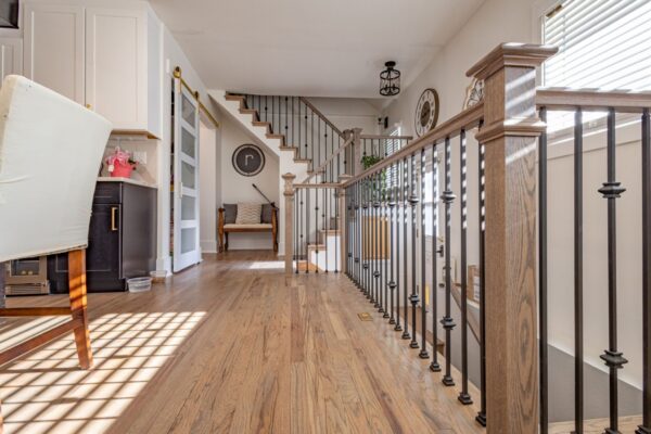 New Build. Interior image of main floor highlighting functional and elegant banisters, stairway to upper and lower floors, comfortable seating space under the stairs, open floor plan, beautiful hardwood floors.