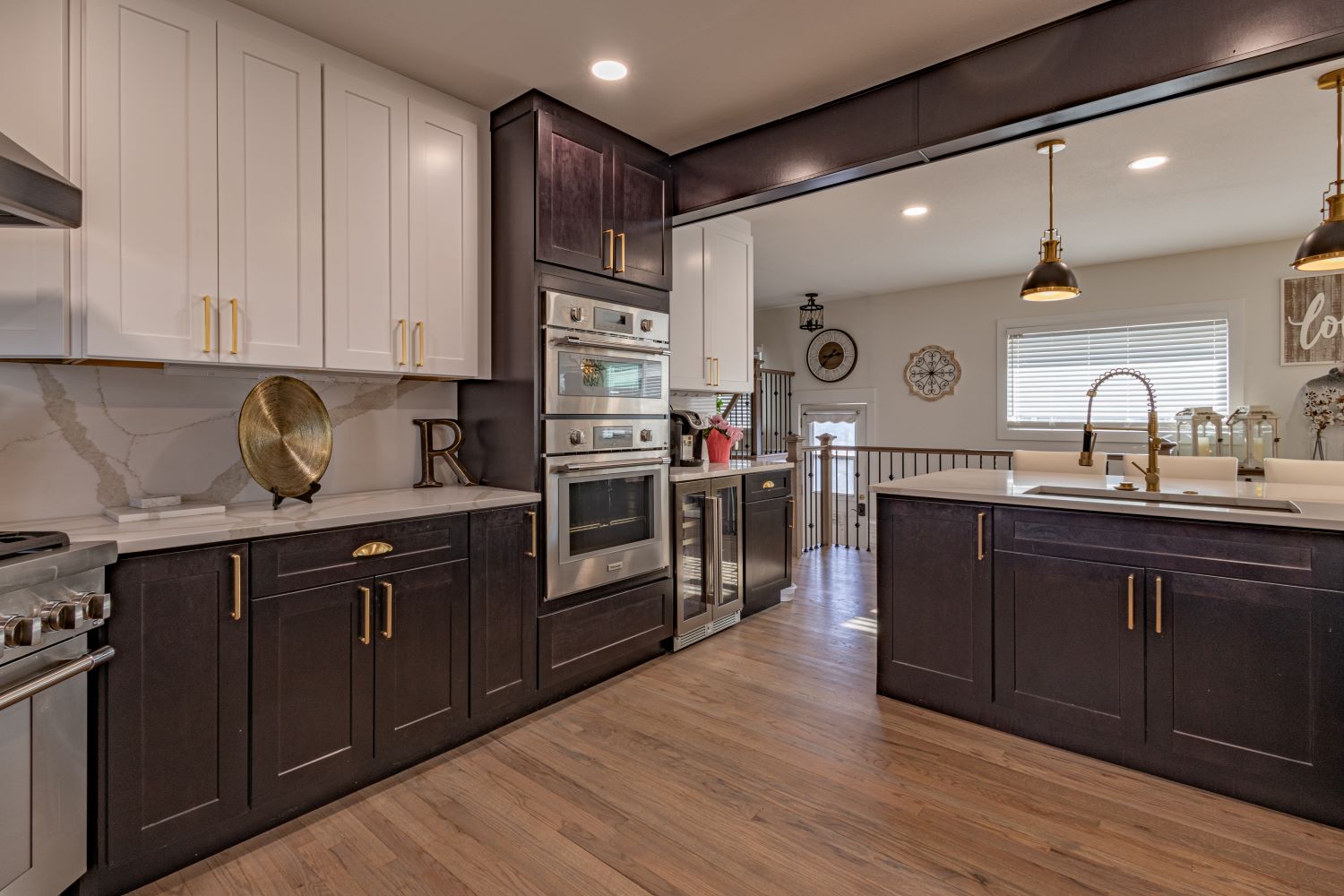 Warm, cozy kitchen with double oven, gas range, island, hardwood floors, elegant fixtures, and banister.